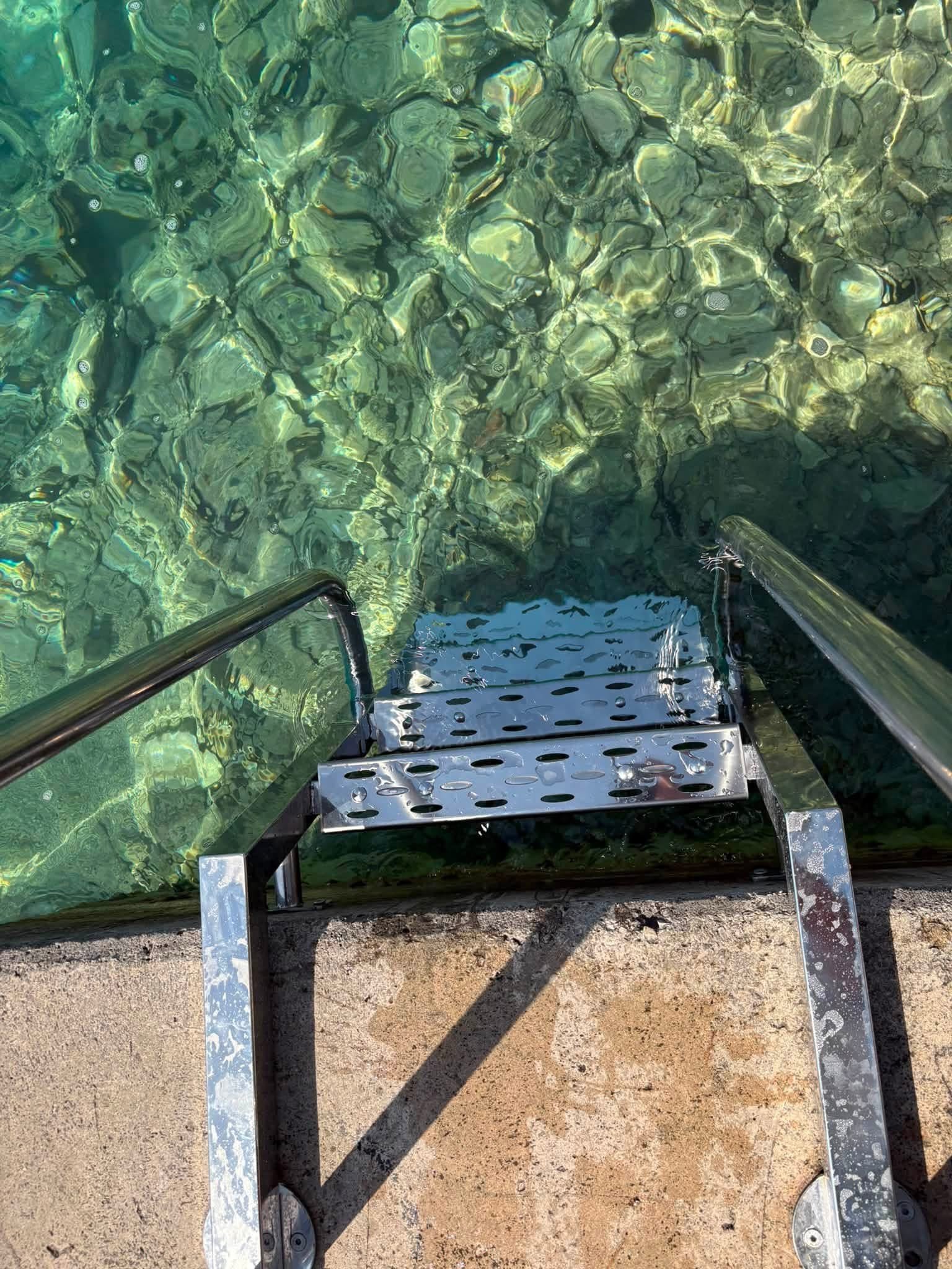 Inox gazište kupališnih ljestava s perforiranim limom, iznad bistrog mora.