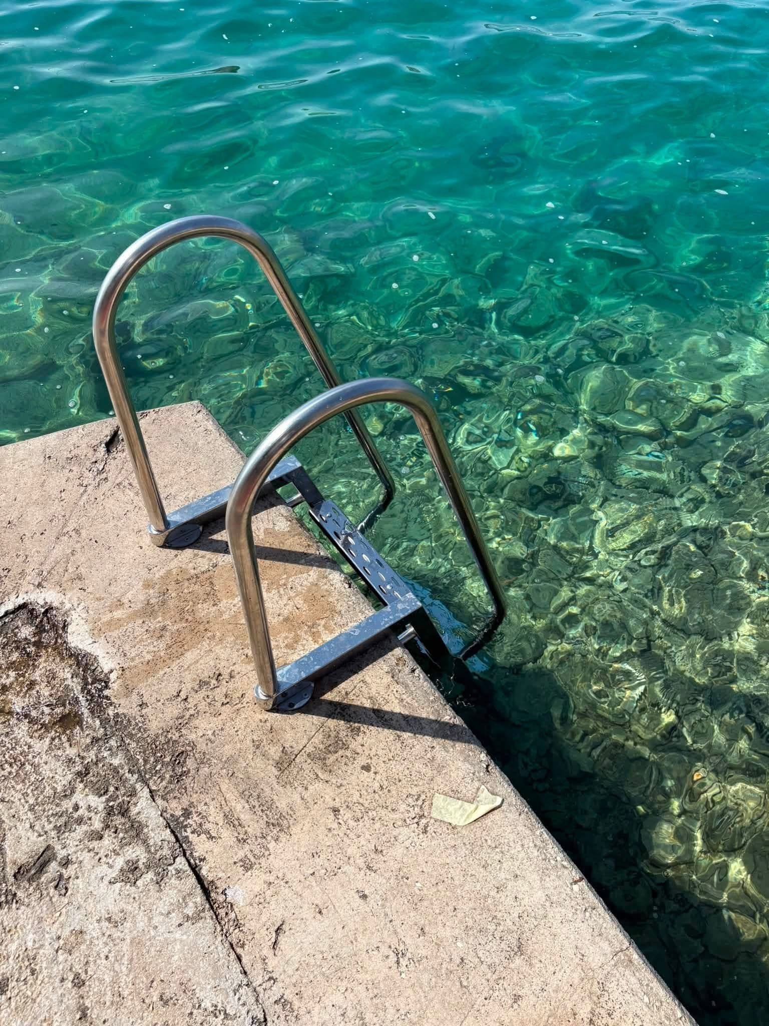 Inox ljestve za ulazak u more pričvršćene na betonsku rivu iznad tirkiznog mora.