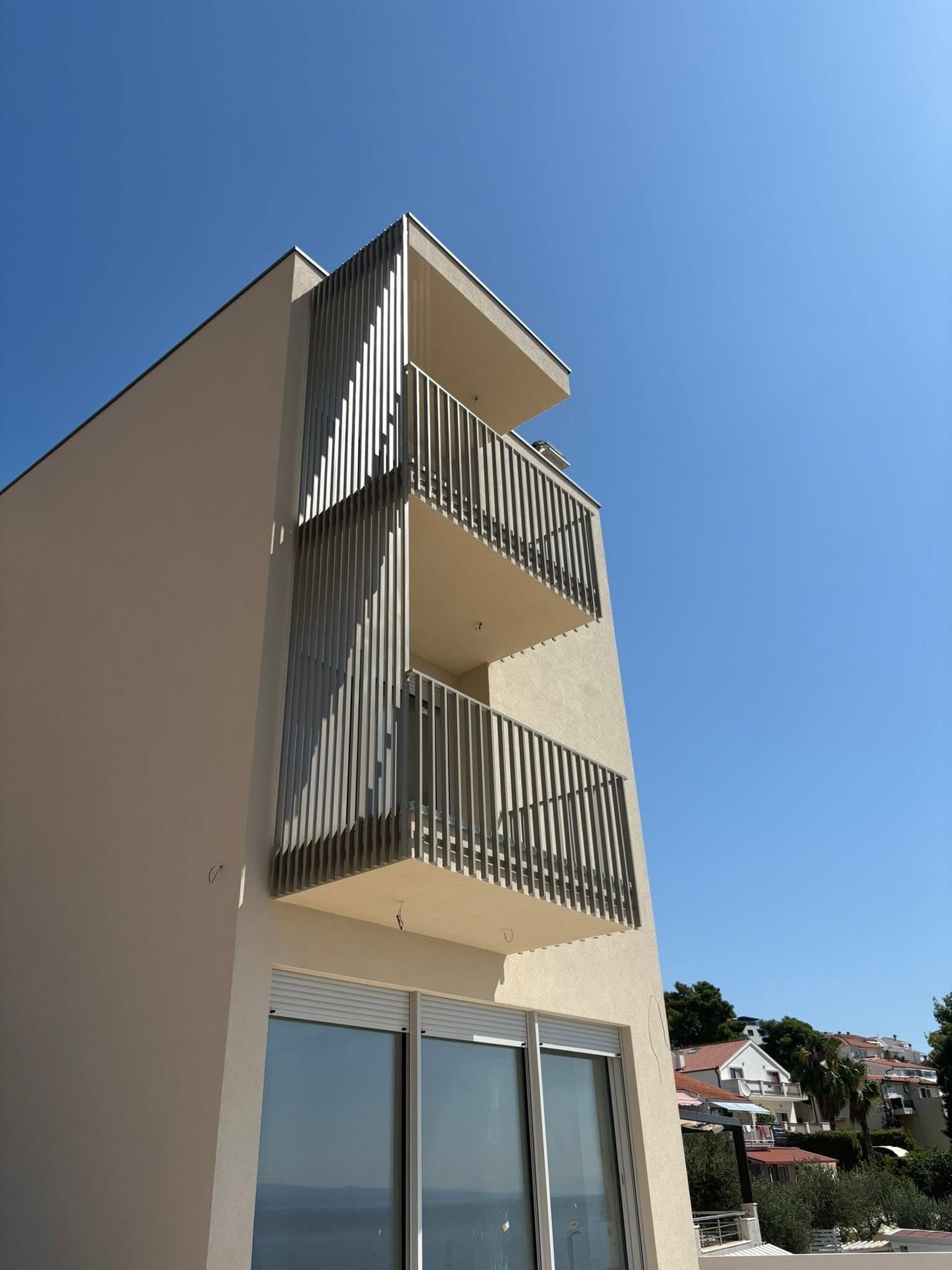 Ugao stambene zgrade s tri balkona zaštićena aluminijskim lamelama i pogledom prema moru.