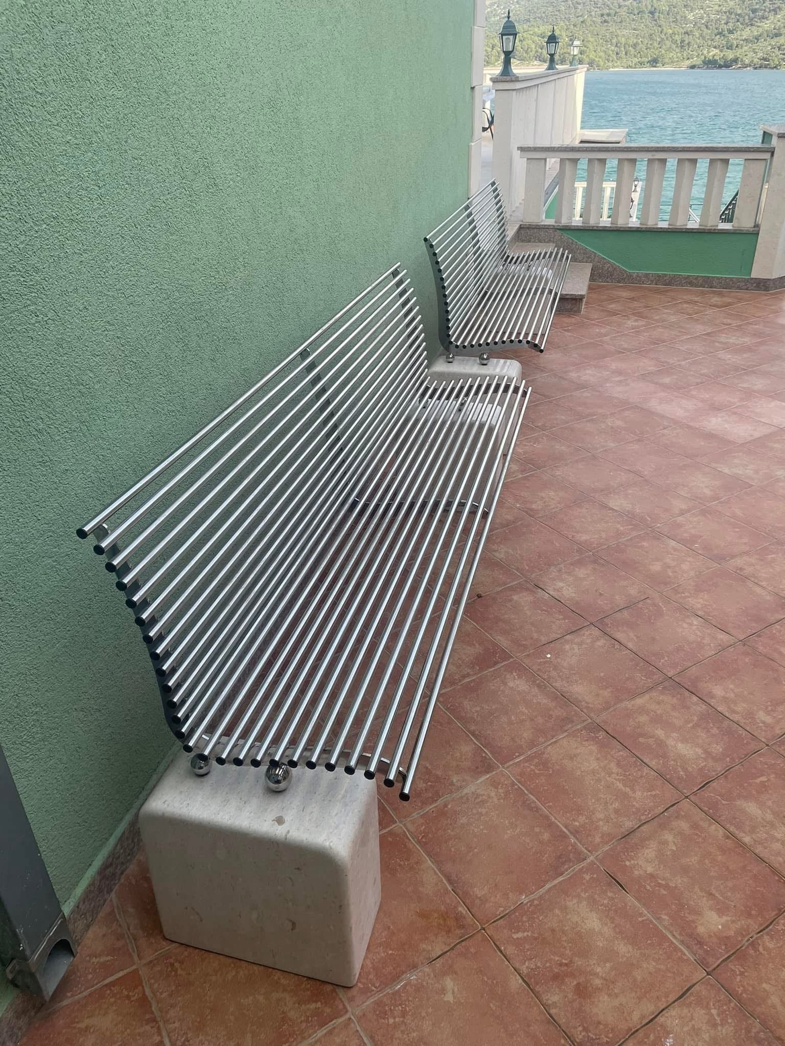 Klupe izrađene od nehrđajućih čeličnih cijevi montirane uz zid terase s pogledom na more.